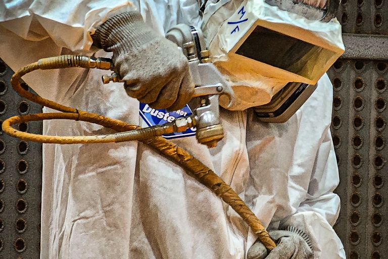 Blasting and painting operator in a full protective suit holding a blast hose