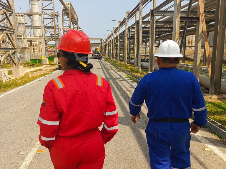 Woman and man in coveralls and hard hats walking along a refinery pipe rack